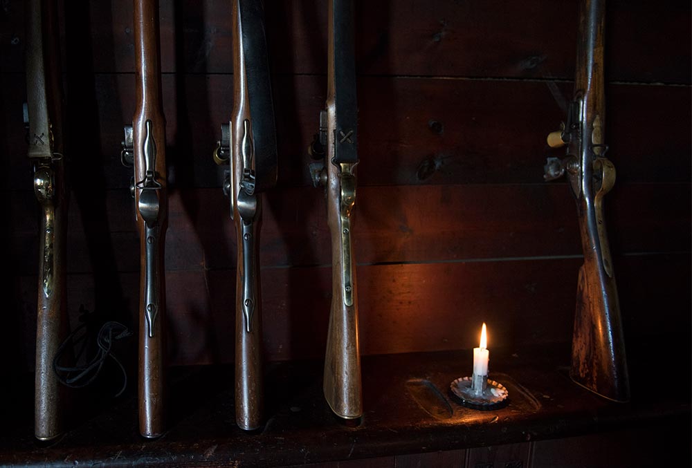 Multiple guns sitting at a gun rack with a lit candle on the right side