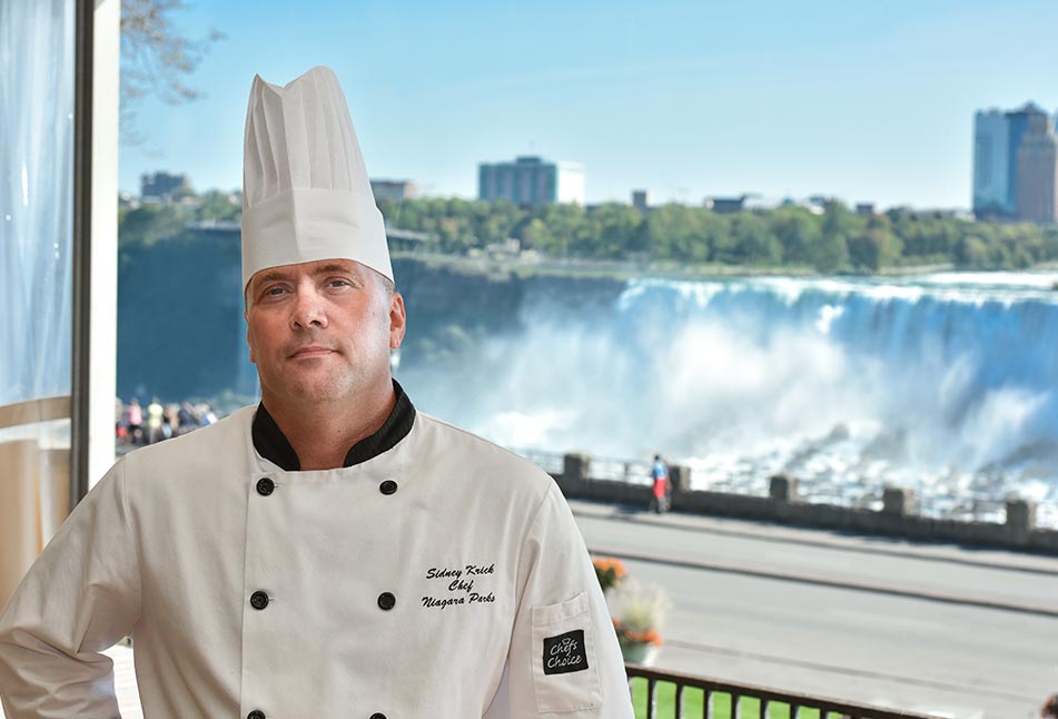 Chef Sidney Krick standing beside a view of the Niagara Falls
